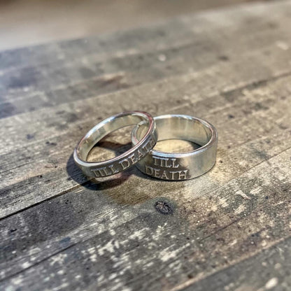 Matching Till Death rings displayed on weathered wood
